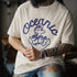 Person wearing a white t-shirt with 'Oceanic Time' design and tattoos on arms.